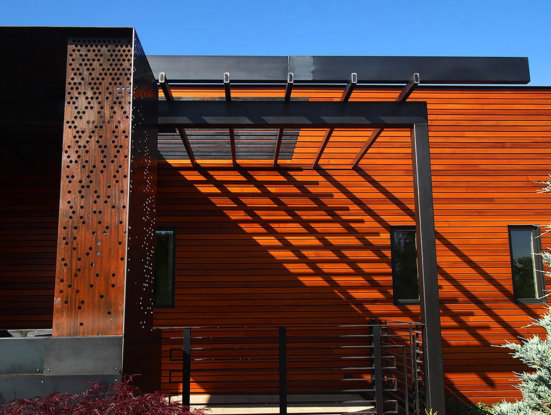 Perforated weathering steel screen and cedar siding with trellis shadows