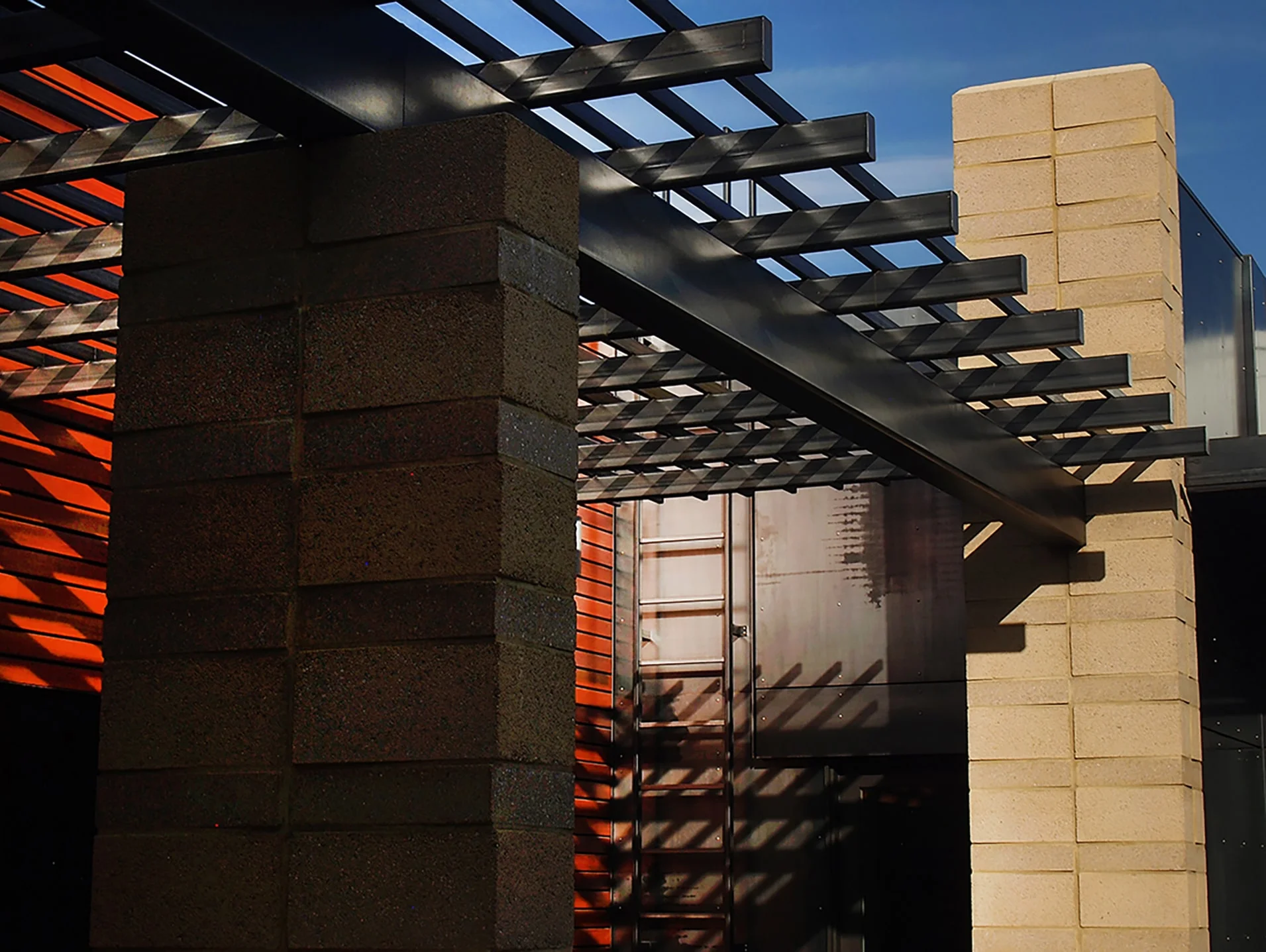Rich block columns and steel trellis casting shadows on cedar siding