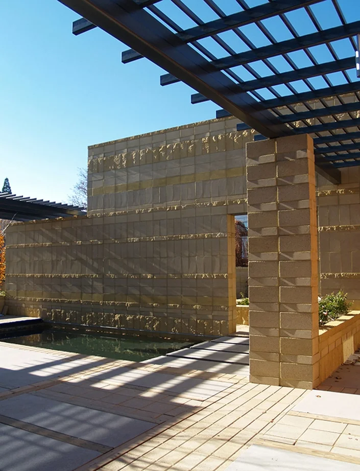 Block garden wall and steel trellis with dappled light on the patio