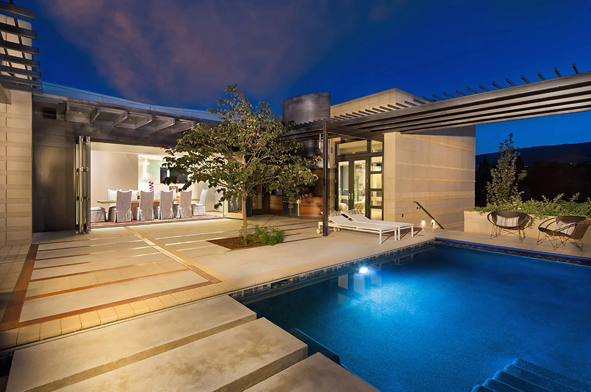 Pool glowing at dusk beside the patio, with the dining room open to the outdoors
