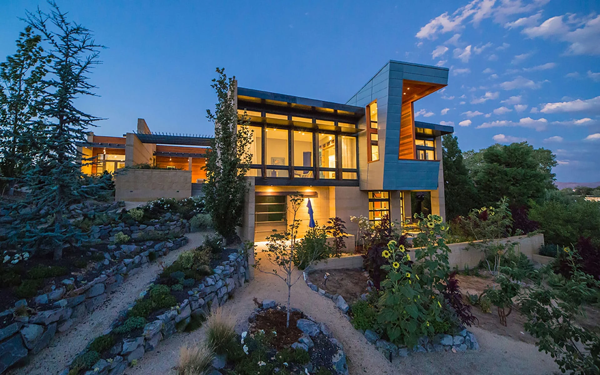 Two-story modern home at dusk above terraced gardens of local plantings