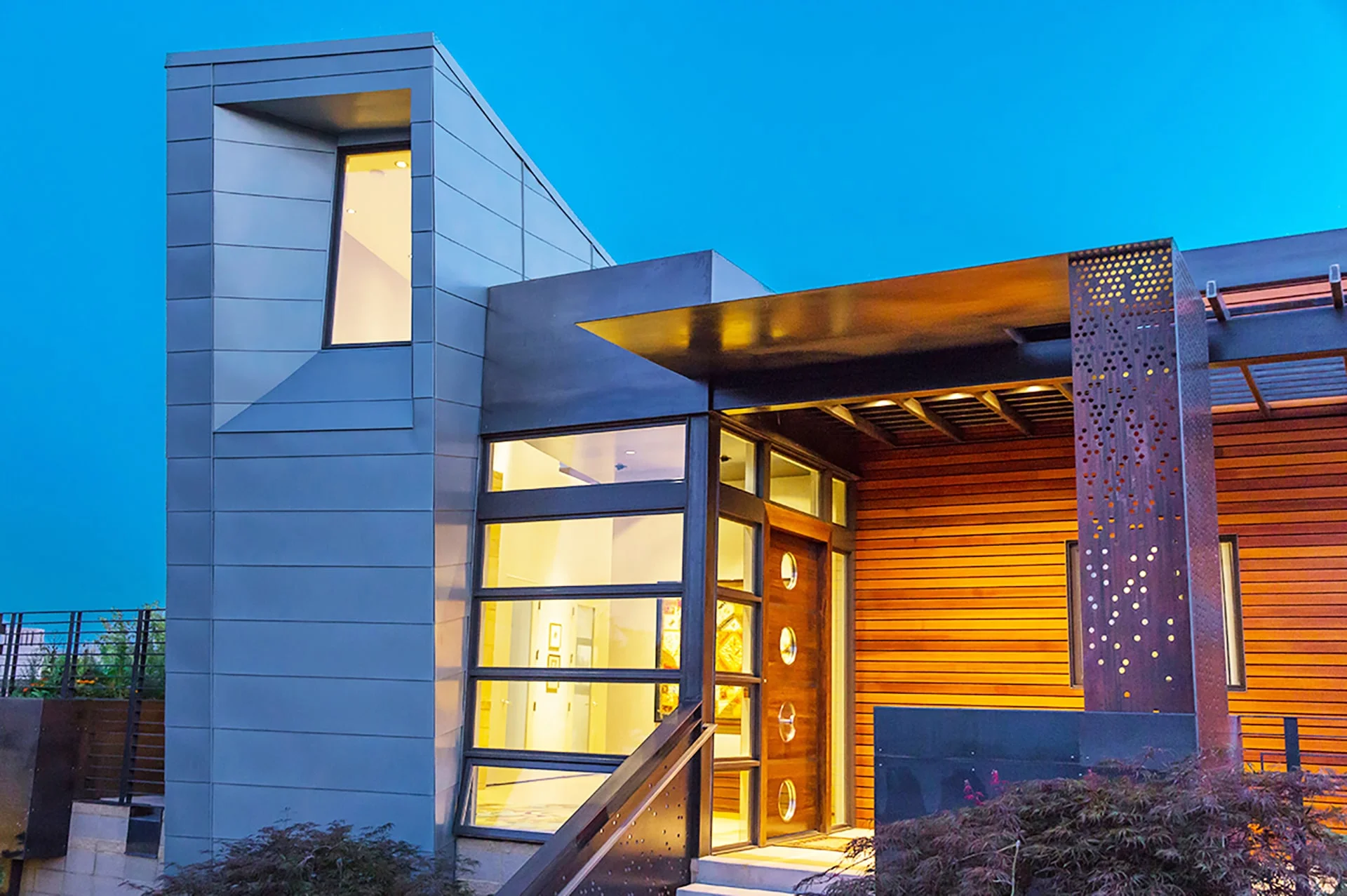 Lit glass entry beneath a steel canopy with a perforated metal screen