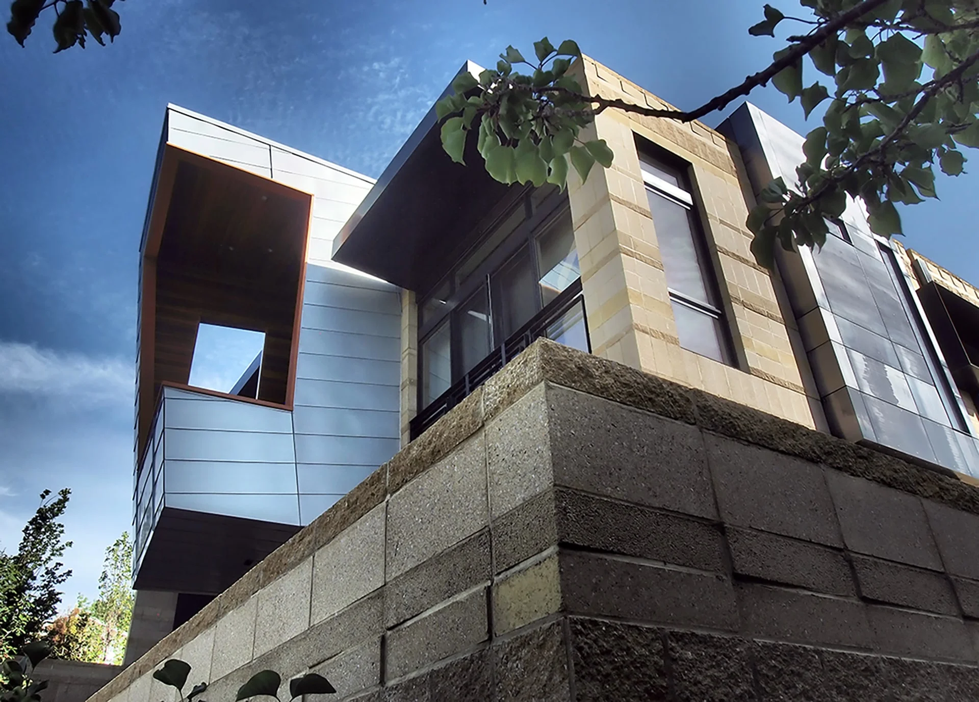 Zinc-clad volumes cantilevering over a stone base against a blue sky