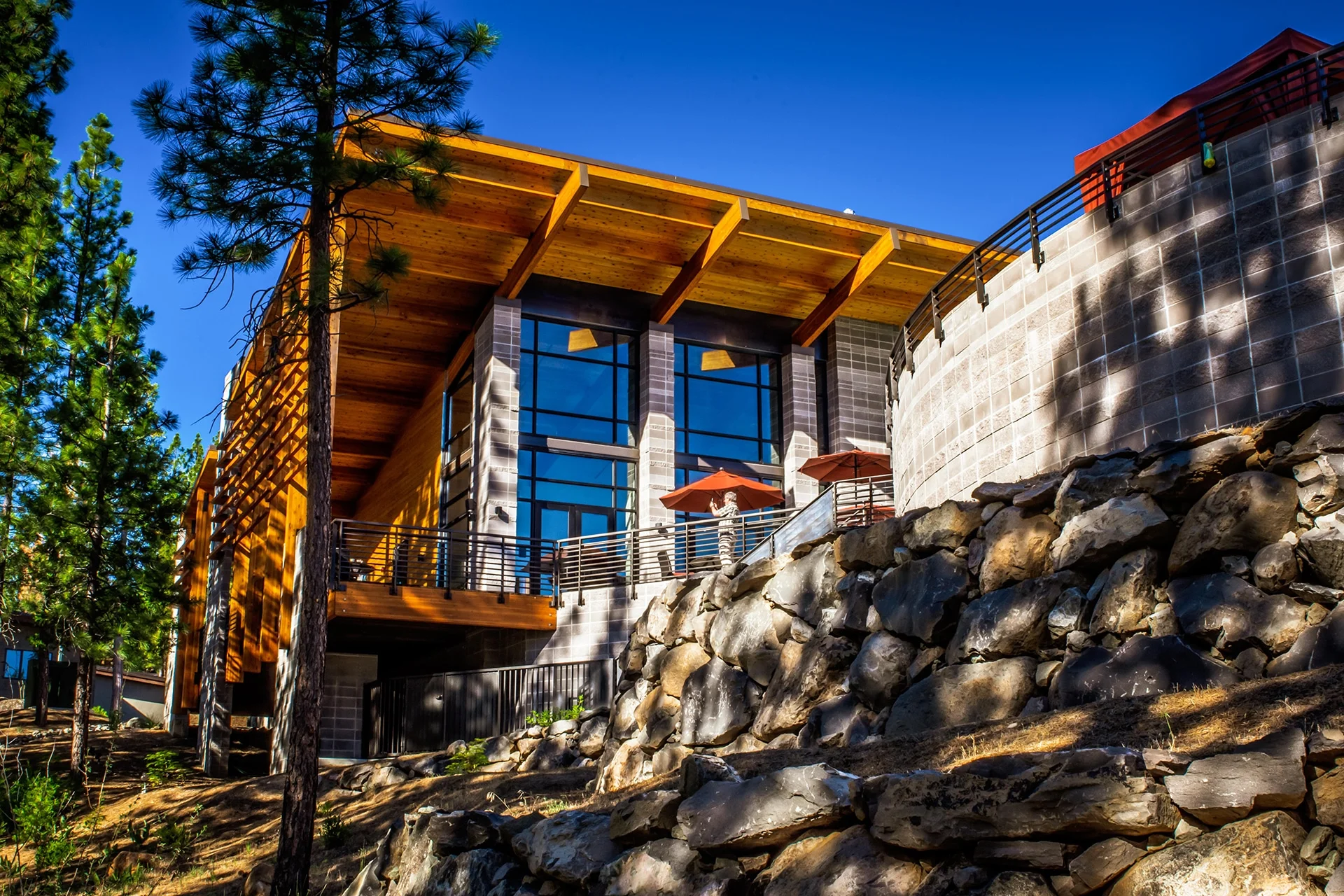 Timber and glass building rising above a boulder retaining wall