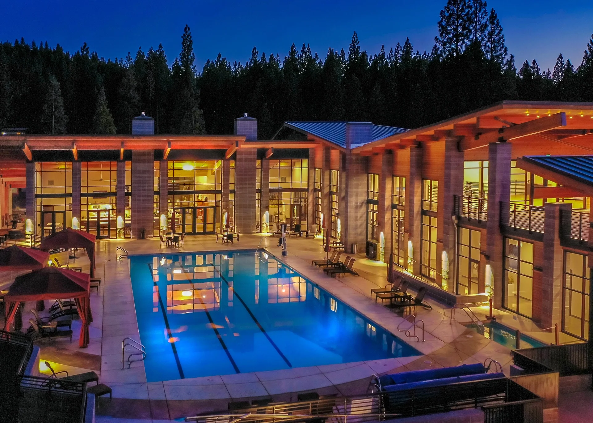 Pool deck at dusk framed by glowing timber-roofed wings and cabanas