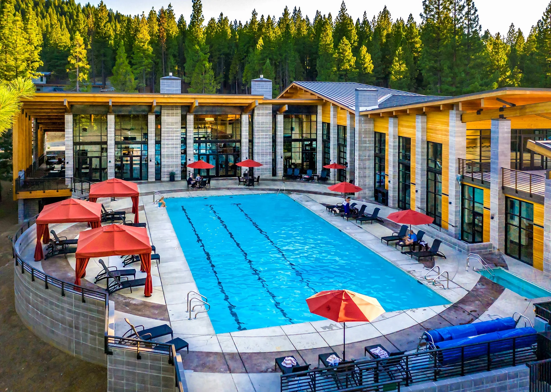 Pool deck with curved rings, red umbrellas, and cabanas against the forest