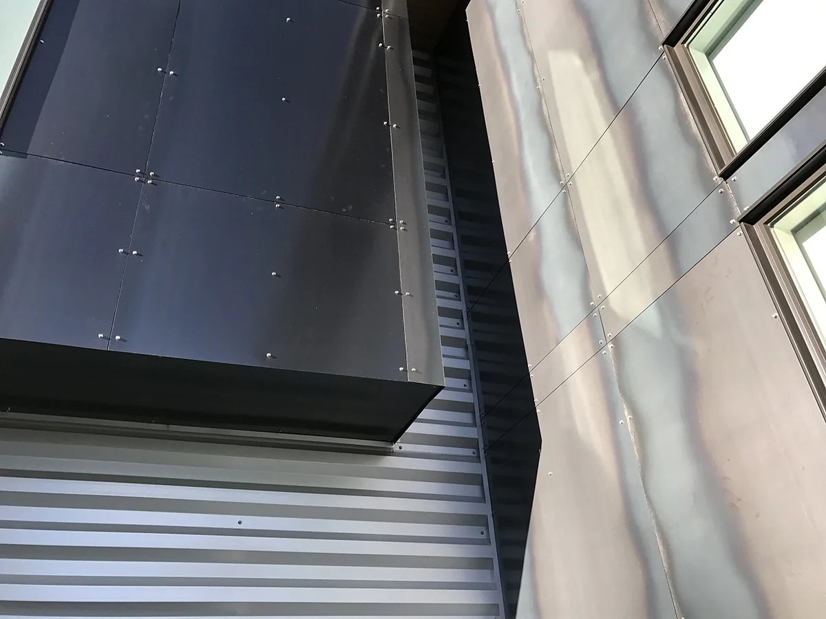 Dark metal panels meeting corrugated metal siding at the corner of the addition
