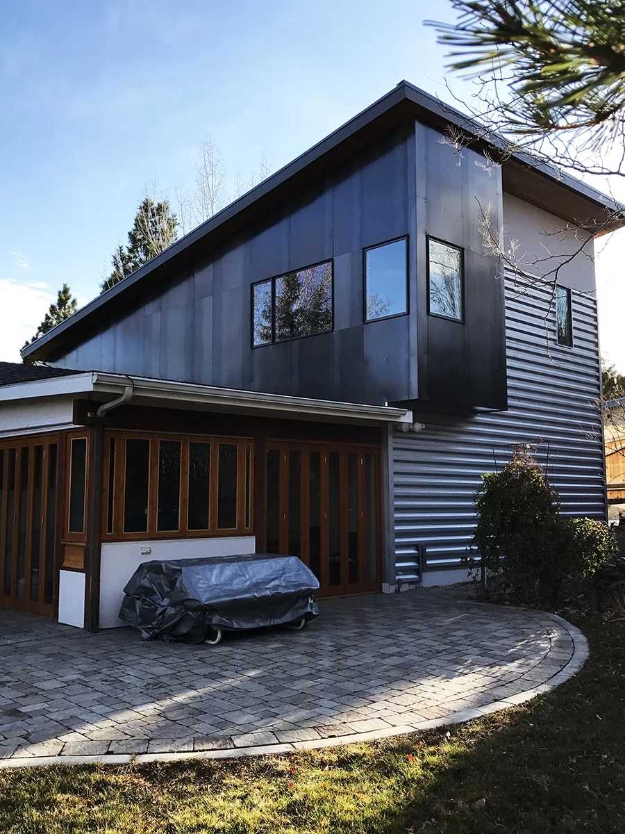 Rear of the home with the new dark metal second floor above a screened porch and paver patio