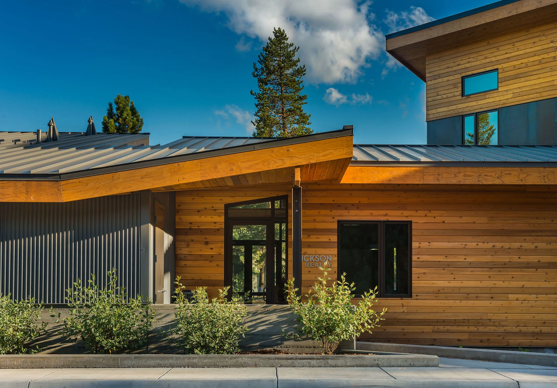 Close view of cedar siding, dark metal panels, and overhanging roof edges under a blue sky