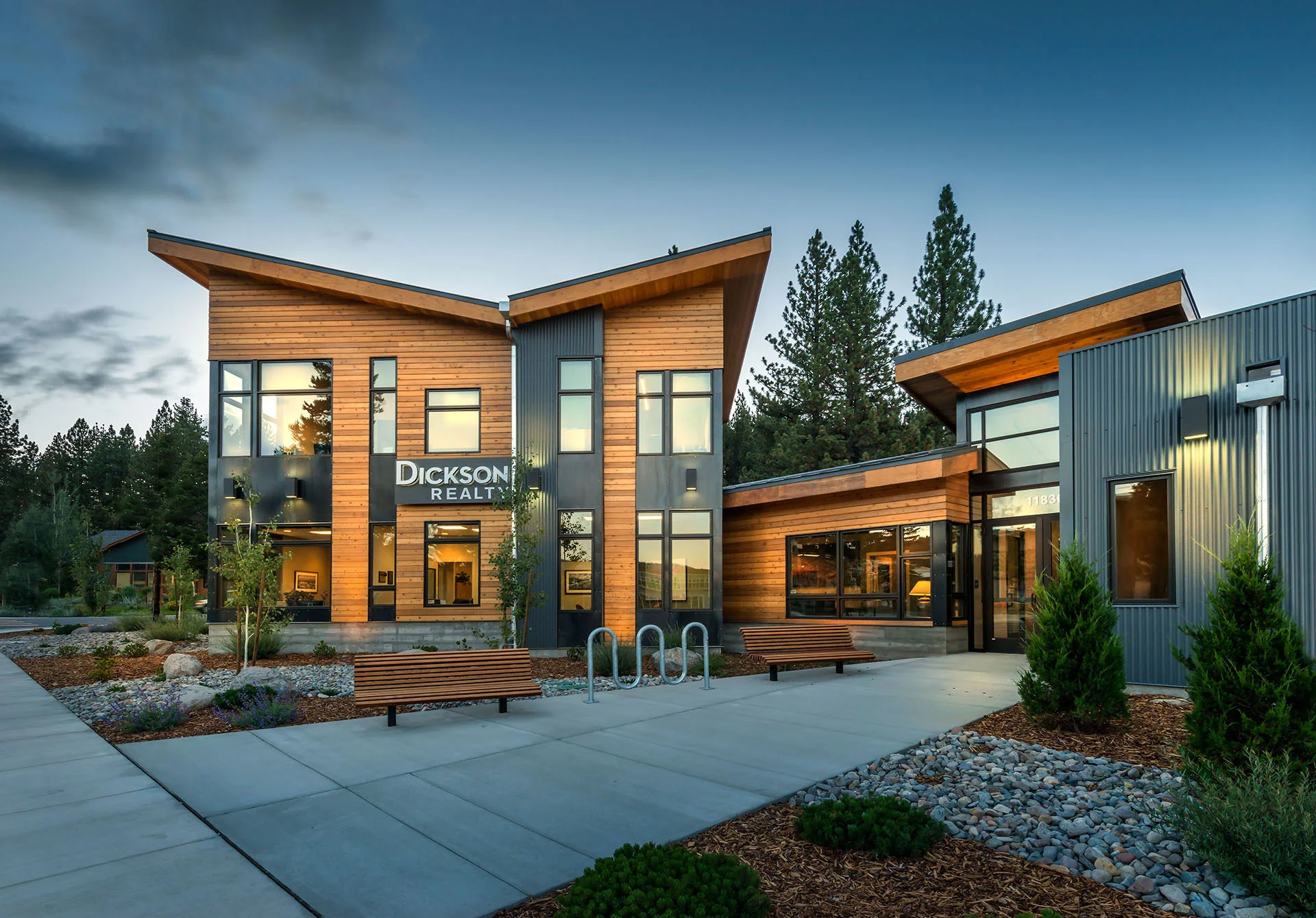 Dickson Realty entry at dusk with glowing windows, benches, and a bike rack
