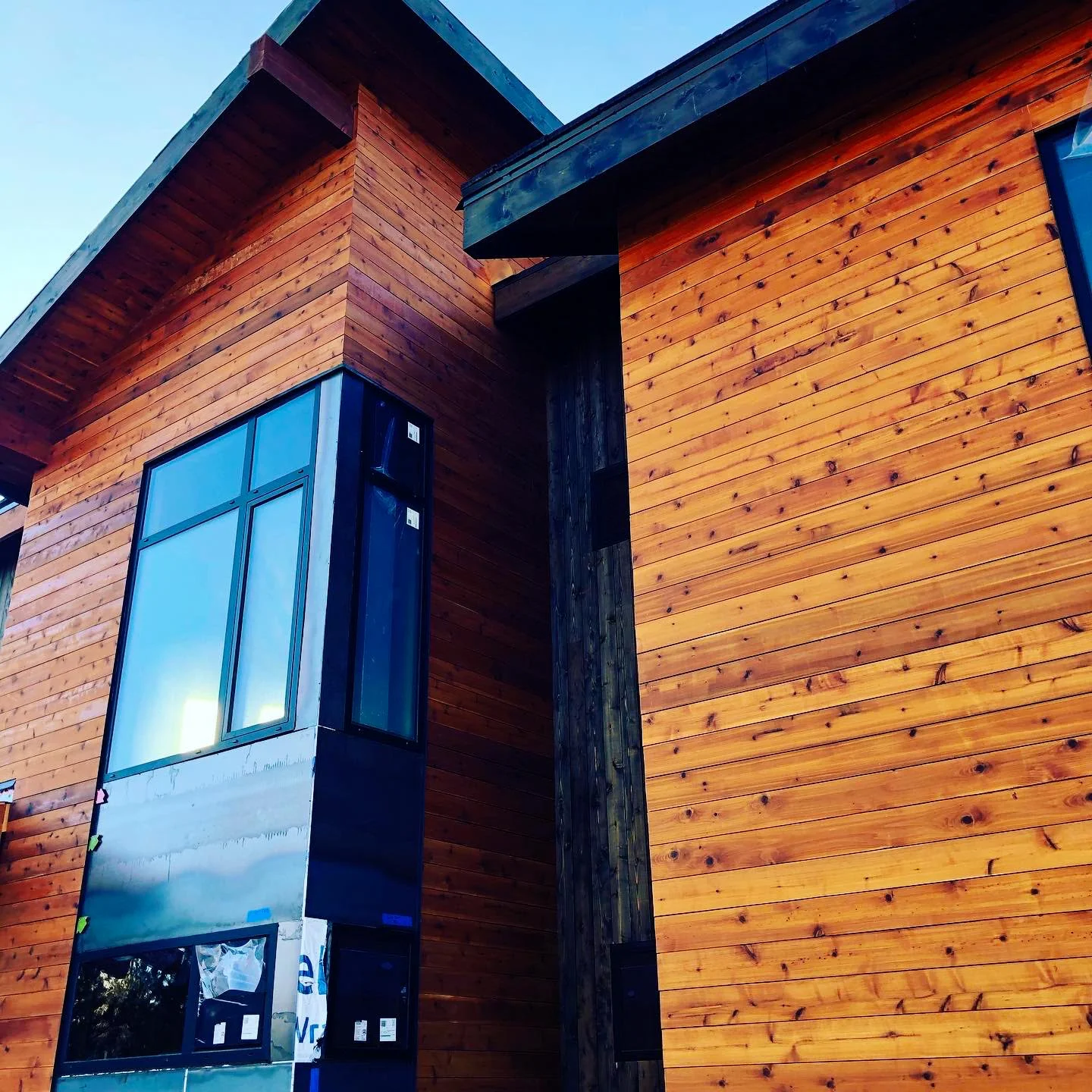 Corner of the house with cedar siding and tall glass windows