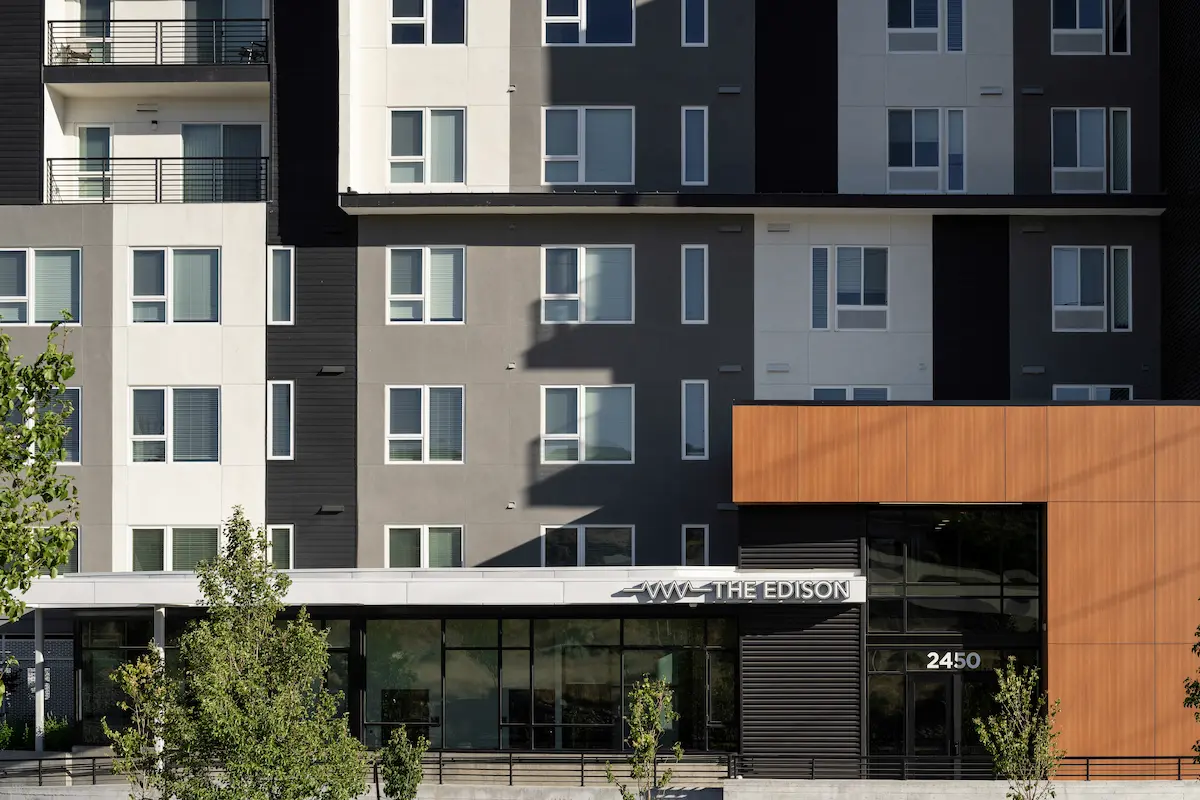 The Edison exterior with dark and light panel facade, burnt orange accent wall, and ground-level storefront at dusk