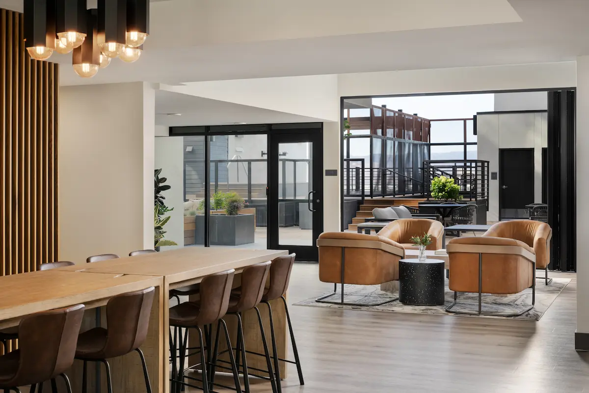 Long communal dining table and lounge seating beside floor-to-ceiling windows