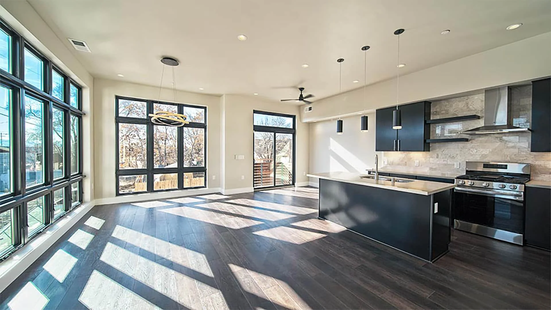 Open living and kitchen level with tall corner windows and dark wood floors
