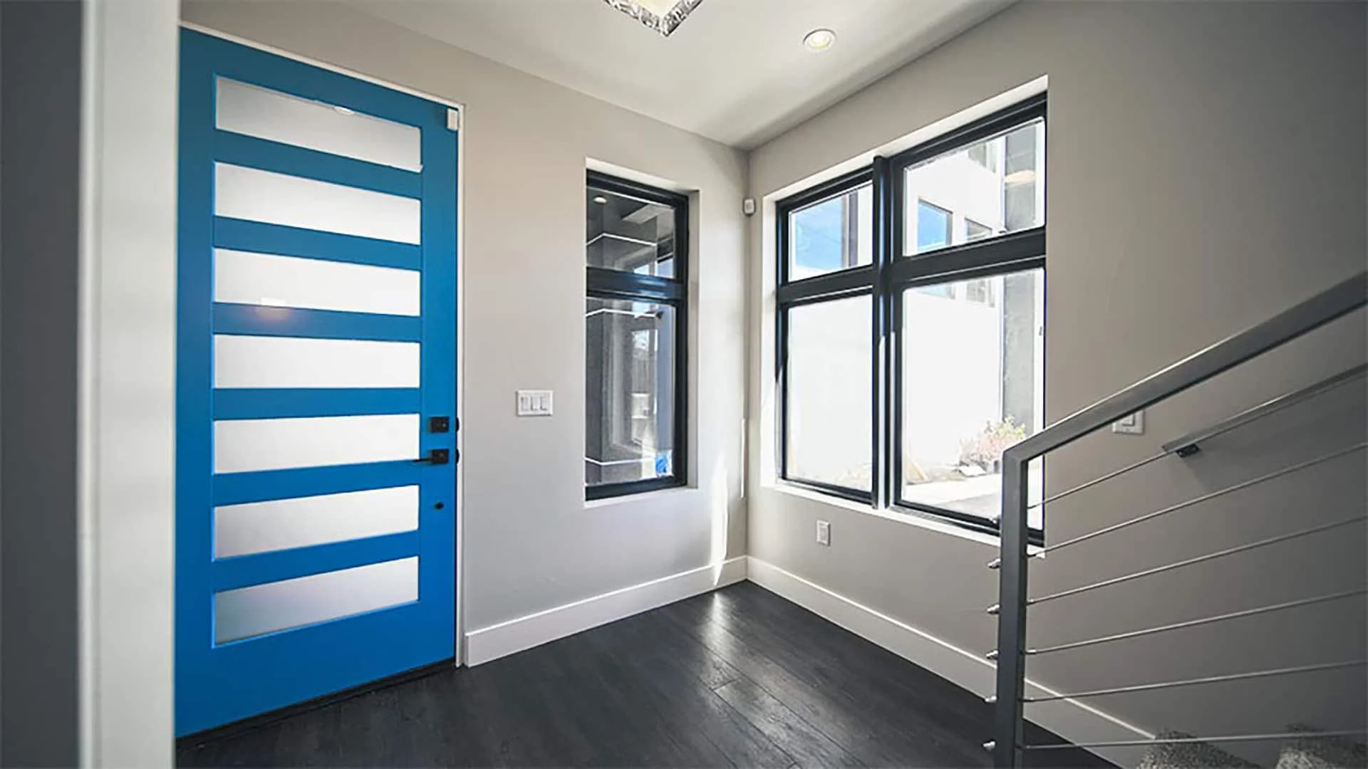 Bright blue entry door with frosted glass panels beside a cable-rail stair