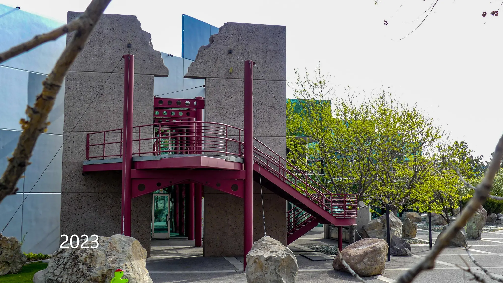 Red steel exterior stair between concrete wall forms, photographed in 2023