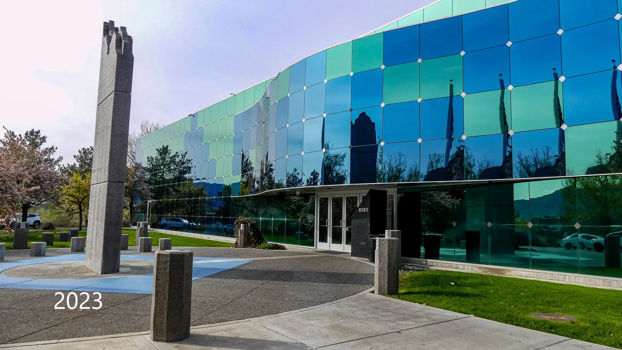 Concrete entry panel in front of the curved mirrored glass facade, photographed in 2023