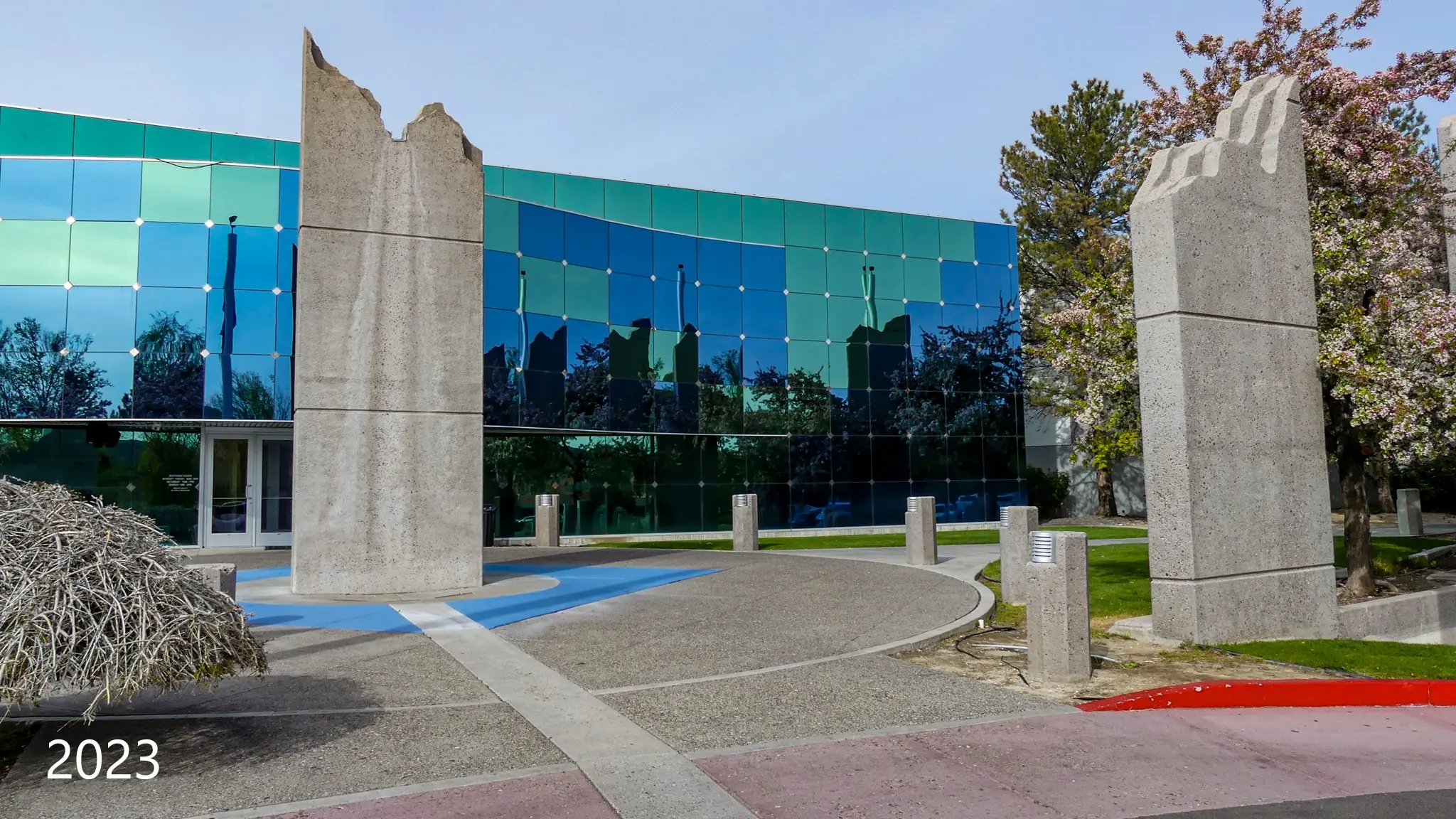 Two towering concrete entry panels in front of the mirrored glass facade, photographed in 2023