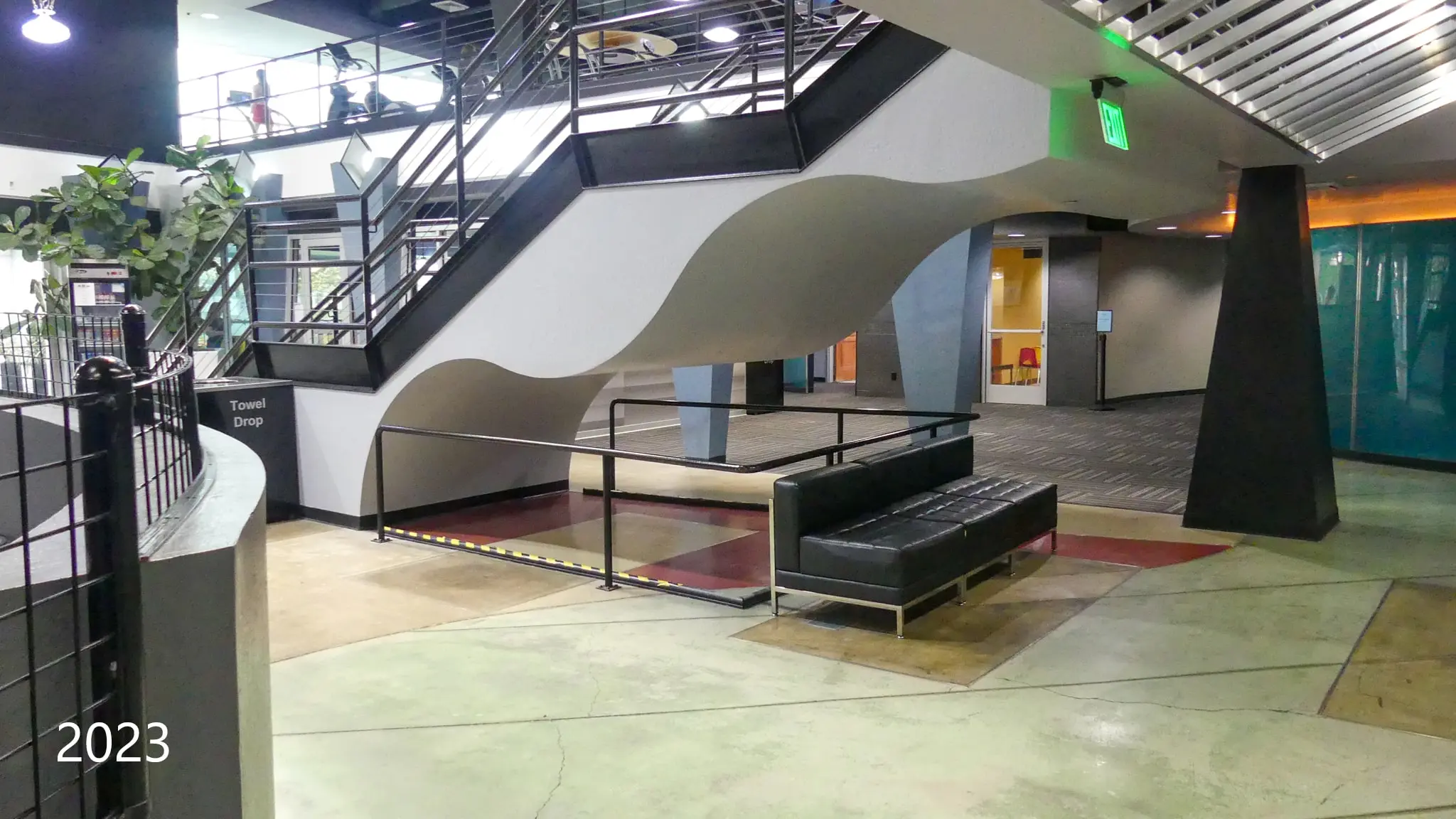 Open interior with a sweeping curved stair and lounge seating, photographed in 2023