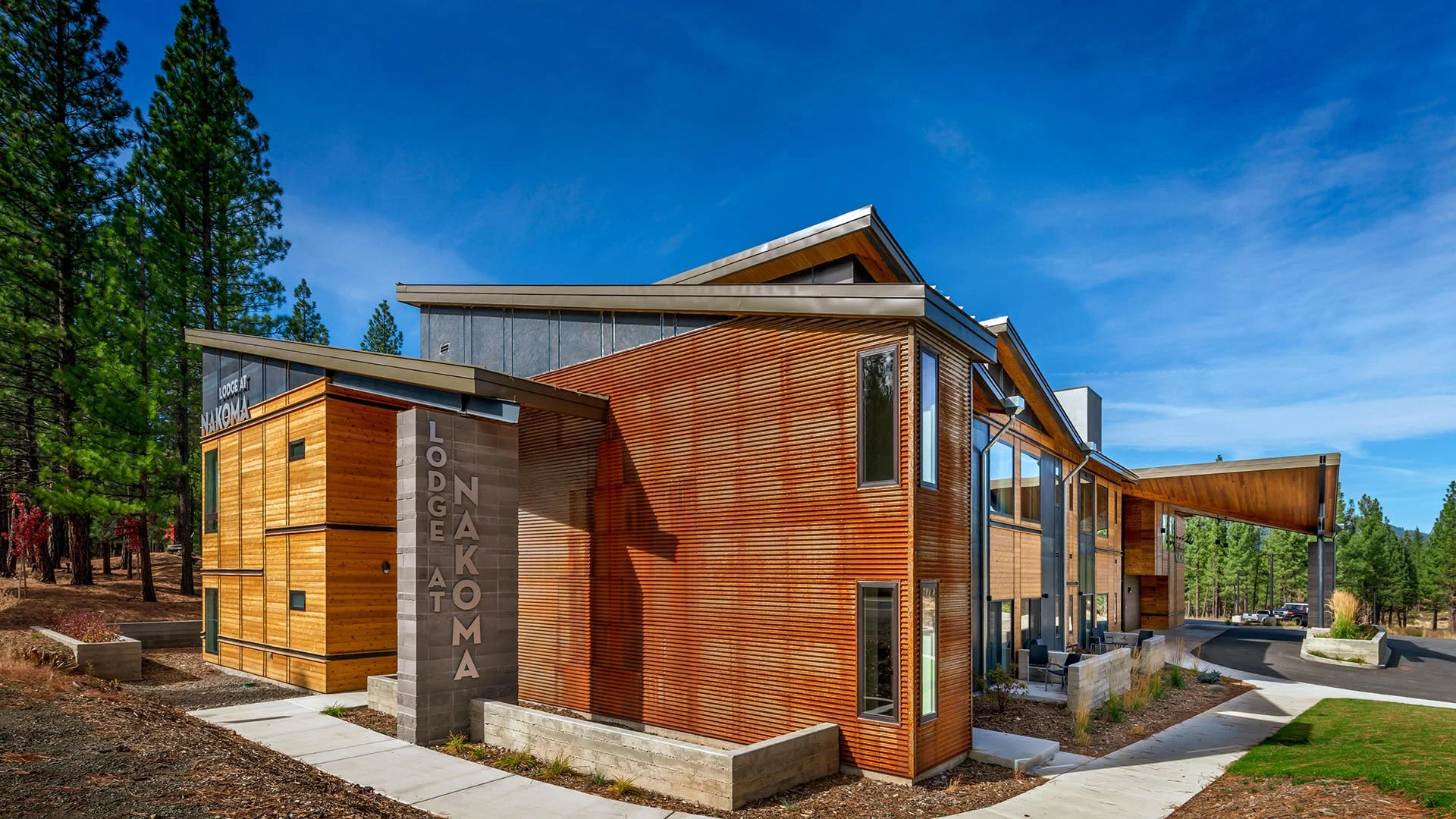 Lodge at Nakoma entry with vertical wood and weathered steel cladding and the Lodge at Nakoma sign, framed by pines