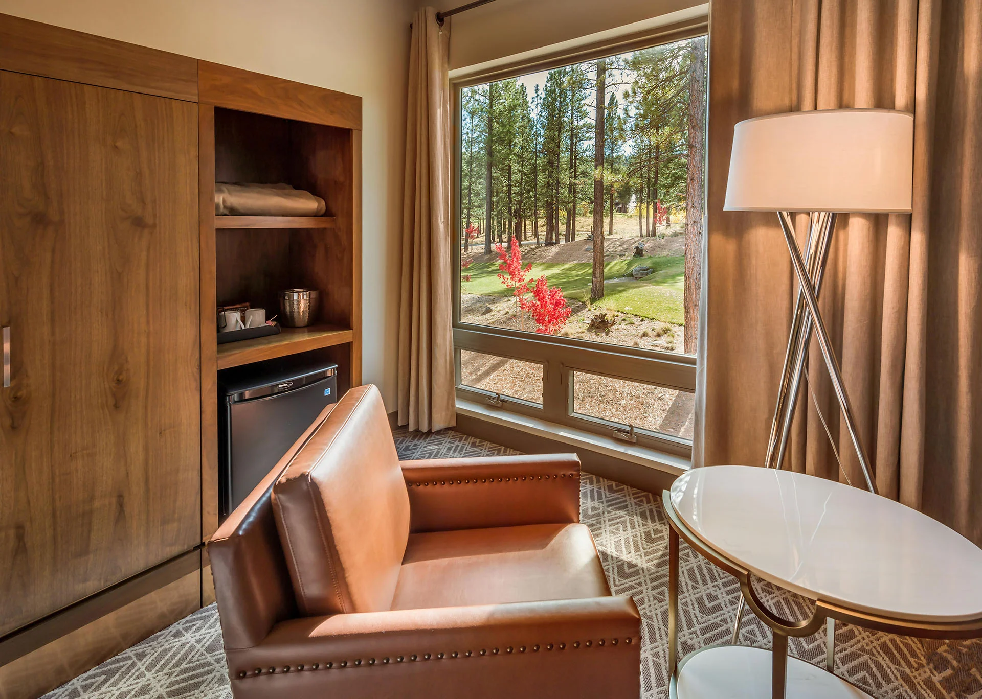 Guest room with a leather chair, side table, and window to the pines