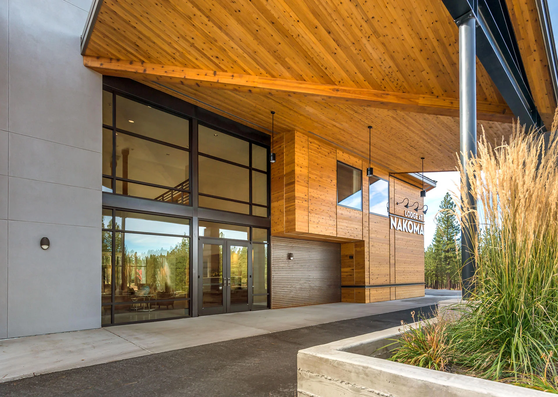 Wood-soffit entry canopy over tall glass doors and native grasses