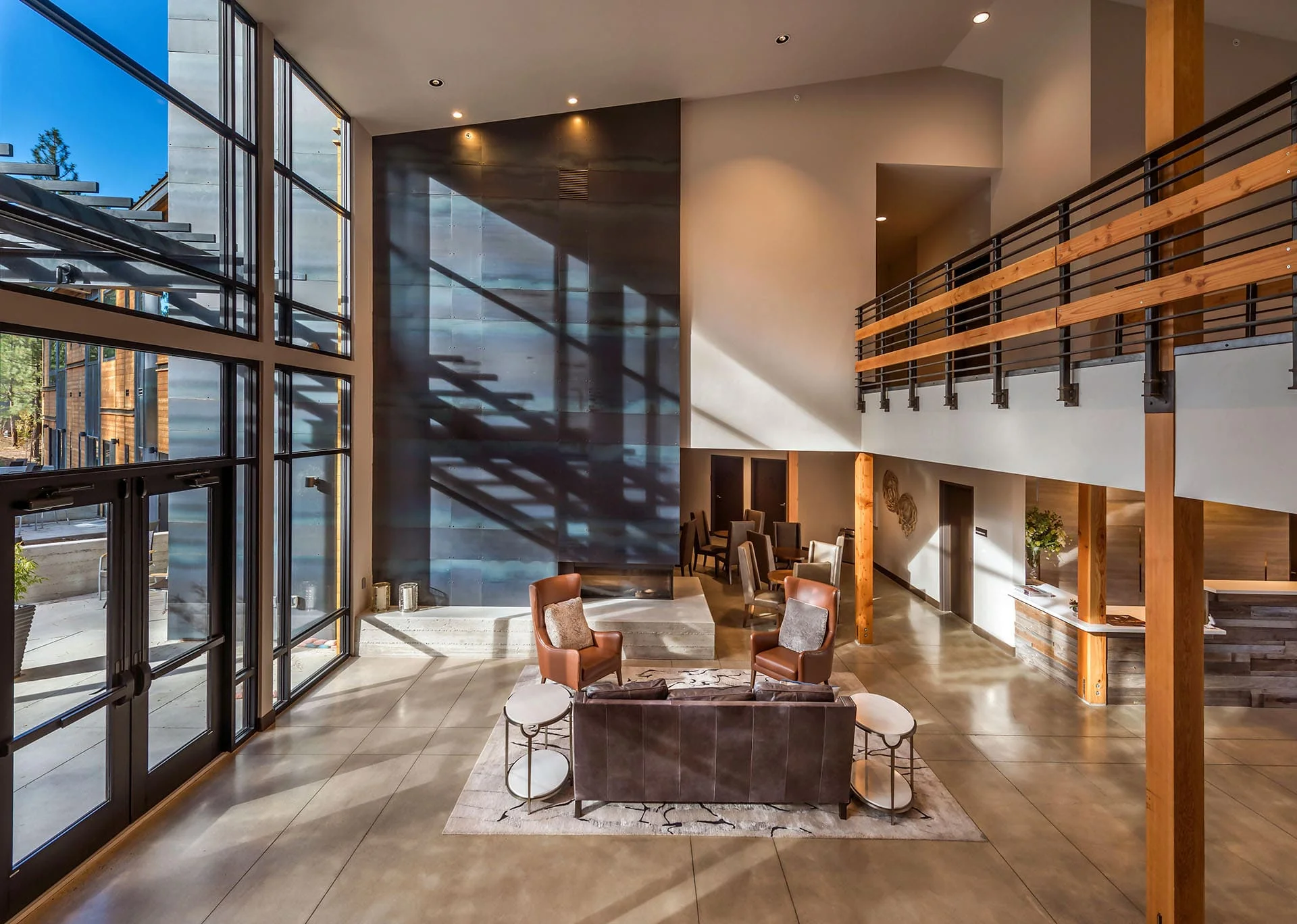 Lobby lounge beneath a mezzanine with tall glazing and a dark feature wall