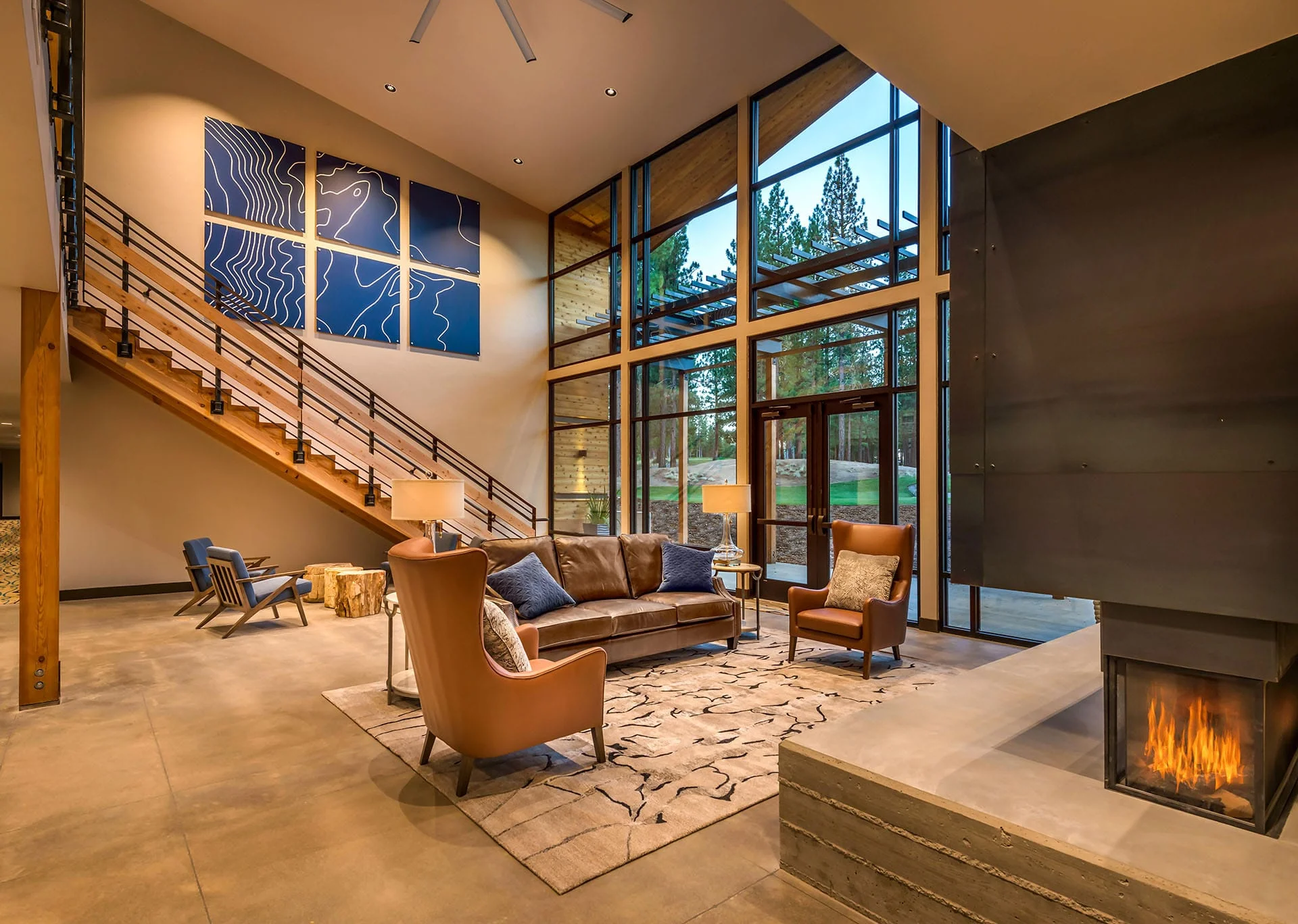 Double-height lounge with leather chairs, a fireplace, and blue artwork beside a wood stair