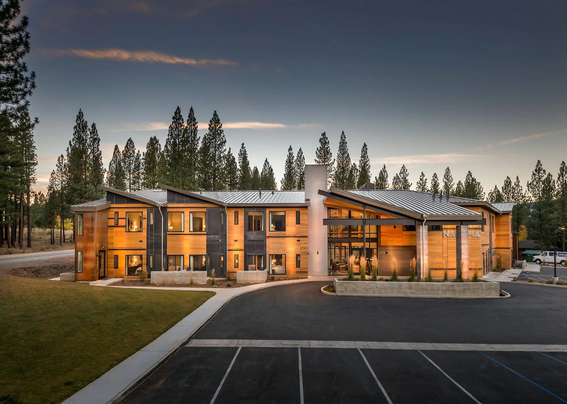 Lodge at Nakoma at dusk with glowing windows beyond the entry drive and pines
