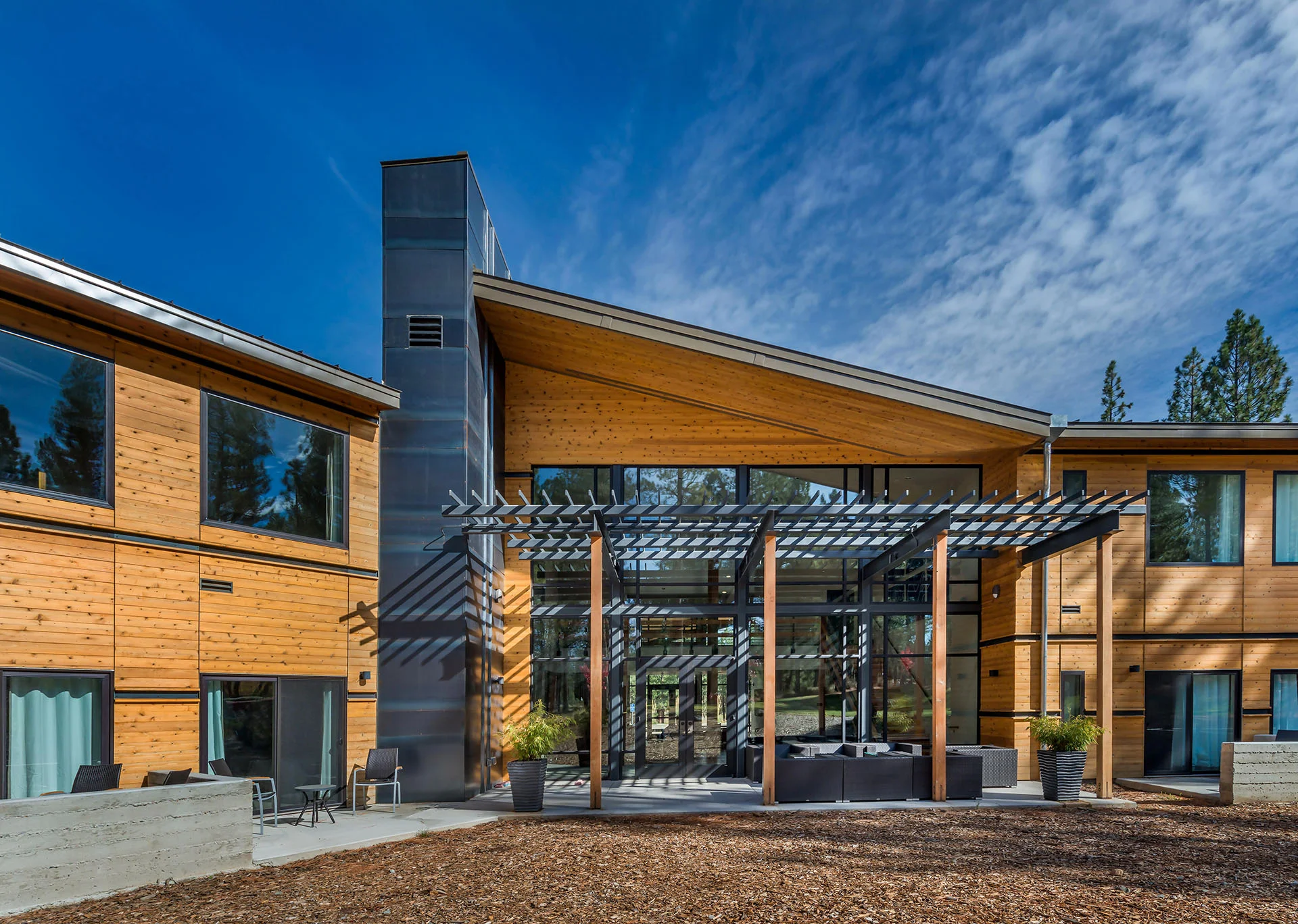 Steel pergola and wood-clad wings around a courtyard under a blue sky