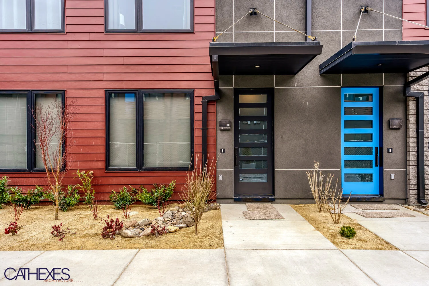 Townhome entries with a bright blue front door, red siding, and dark stucco along the sidewalk