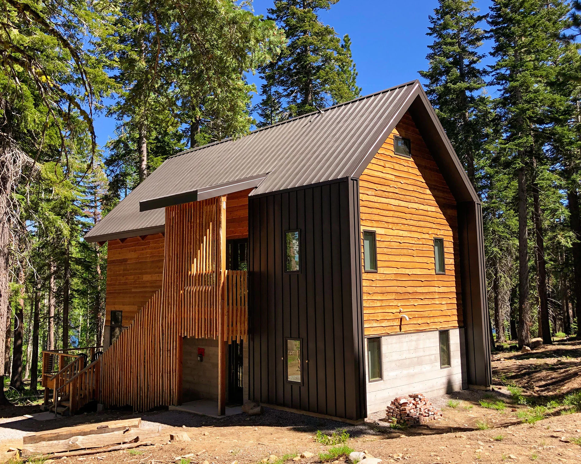 Cabin with dark metal and cedar siding and an exterior stair to the upper level