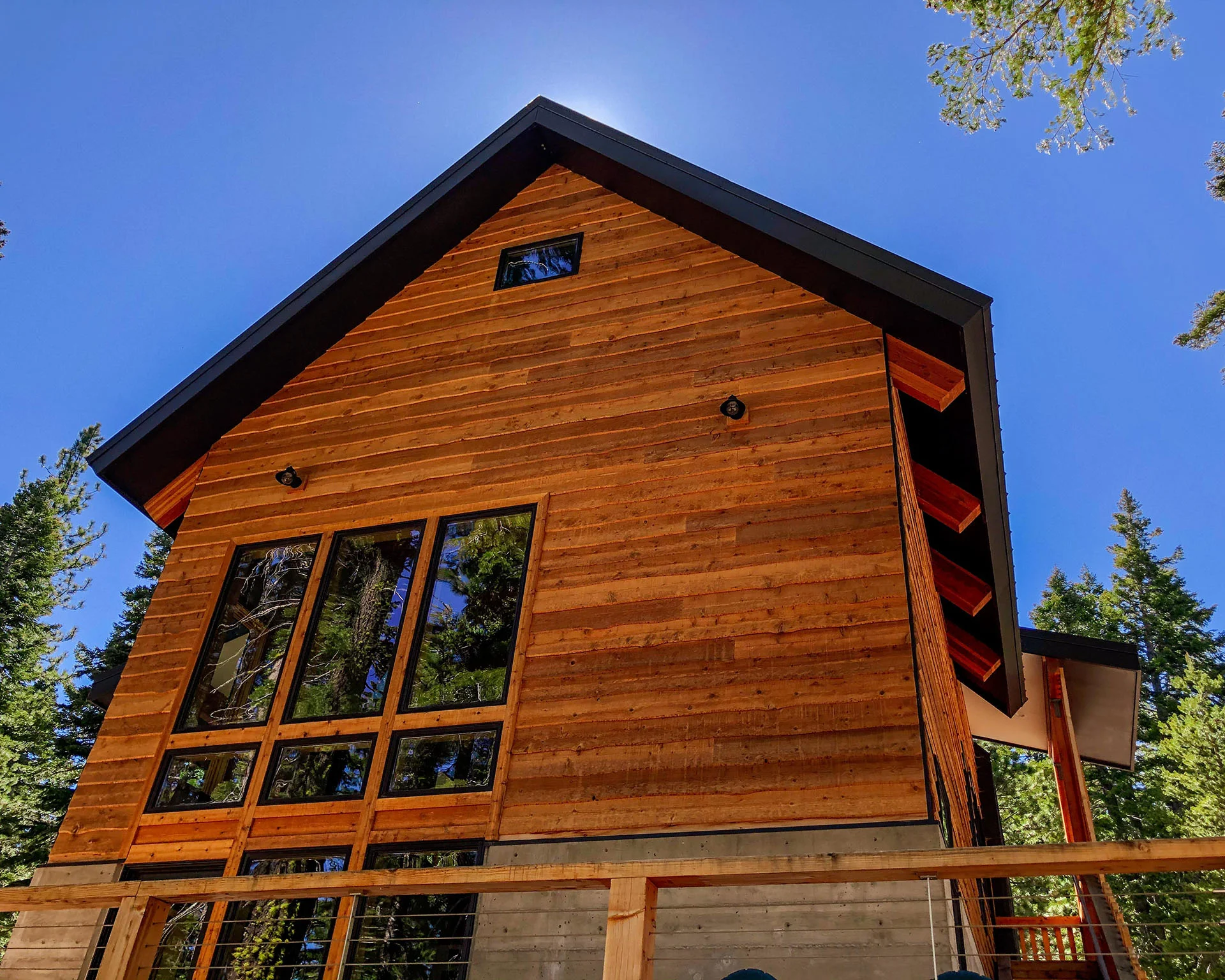 Tall cedar gable with large windows and a steep metal roof against a blue sky