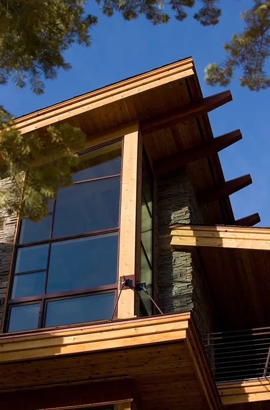 Cedar-clad corner with tall windows and deep overhanging eaves against a blue sky and pine branches