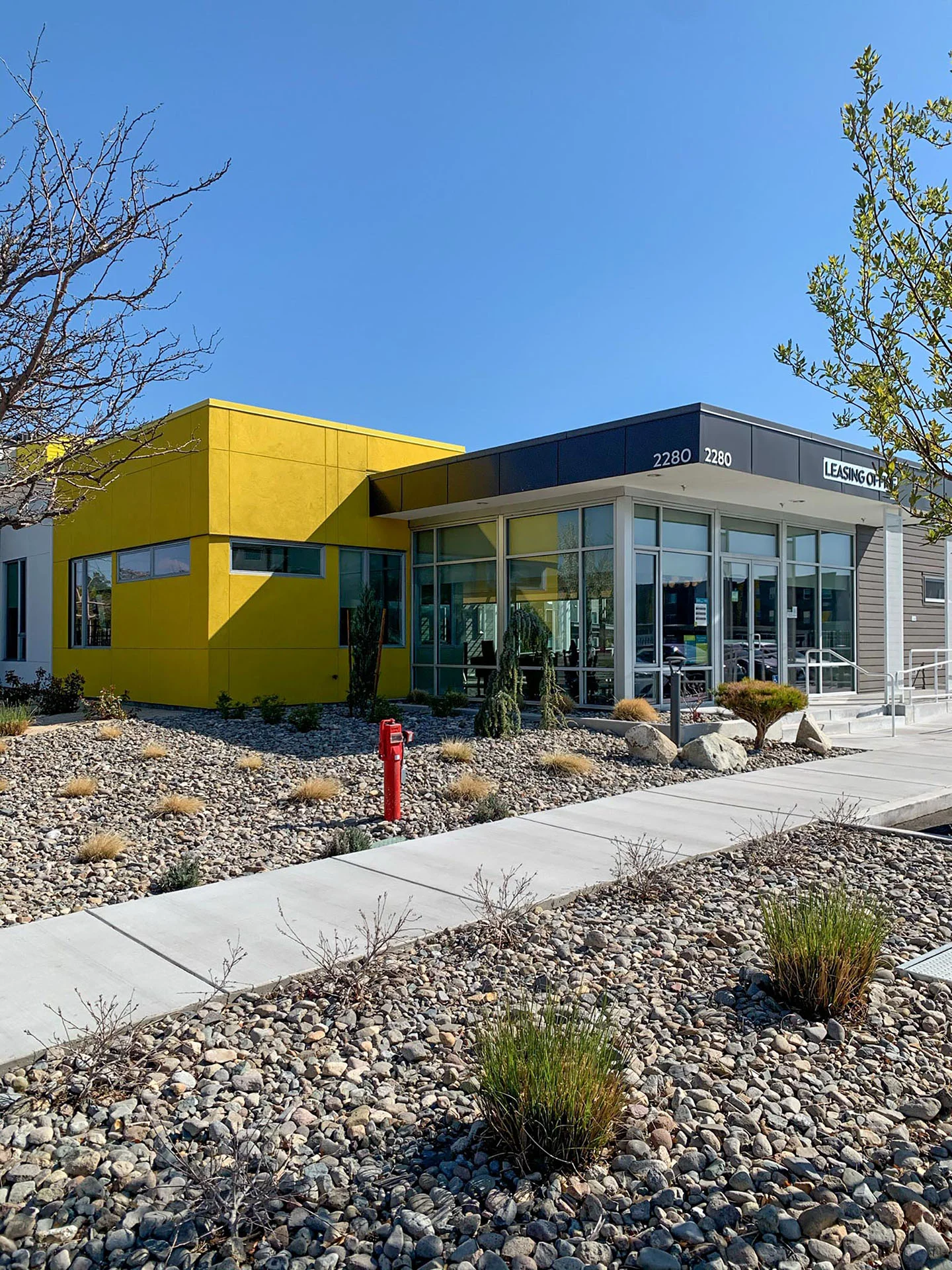 Clubhouse entry with a bright yellow volume and glass storefront beside a landscaped walk