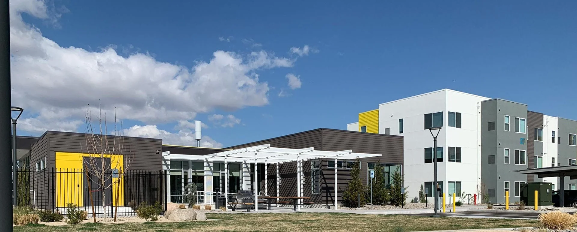 Wide view of the clubhouse, pergola, and lawn with apartment buildings beyond