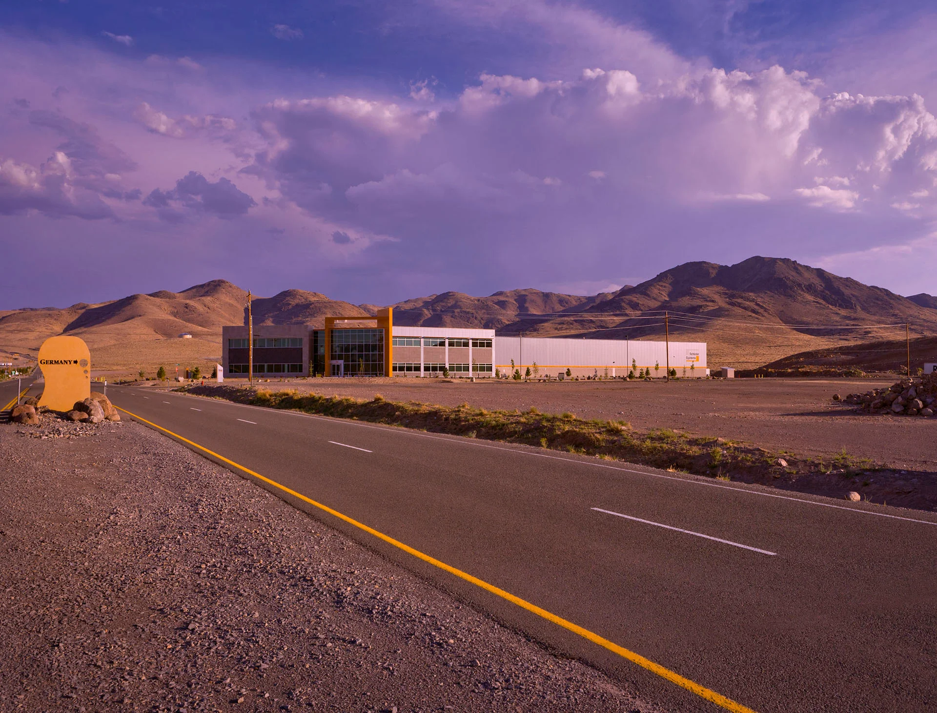 Road leading to the Schluter Systems facility beneath high desert mountains at sunset