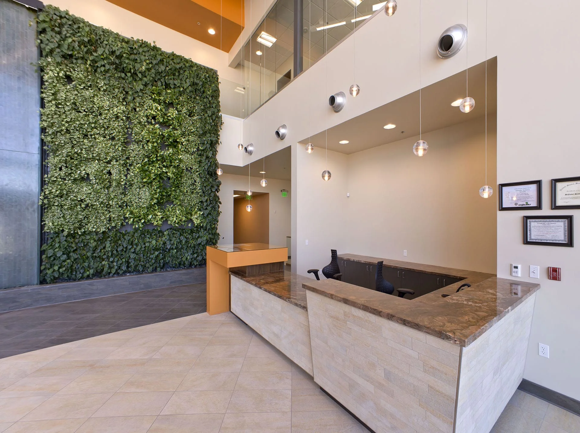 Reception desk beside a full-height living wall under an orange ceiling