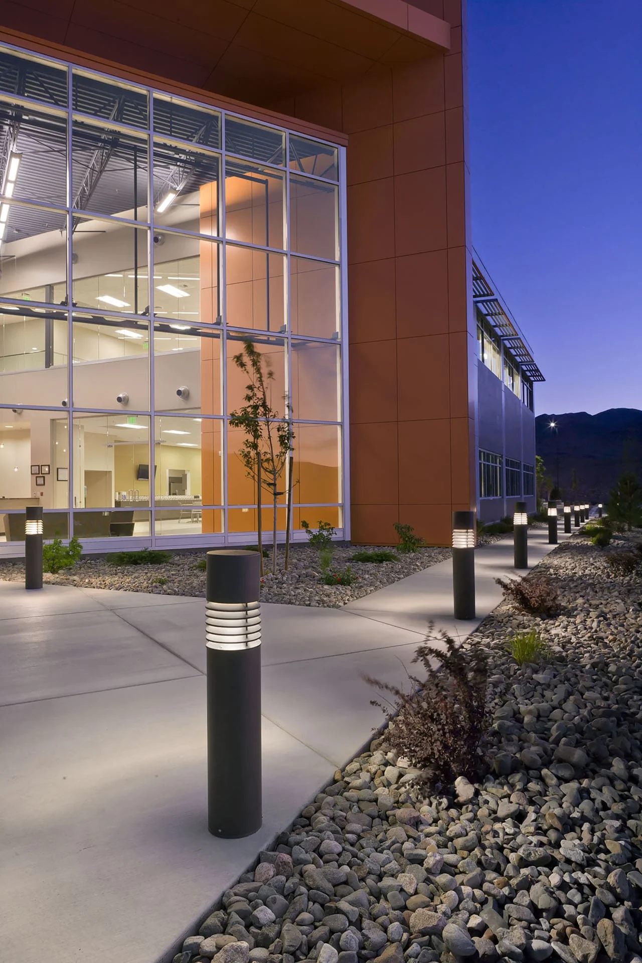 Two-story glass corner of the office lit from within at dusk