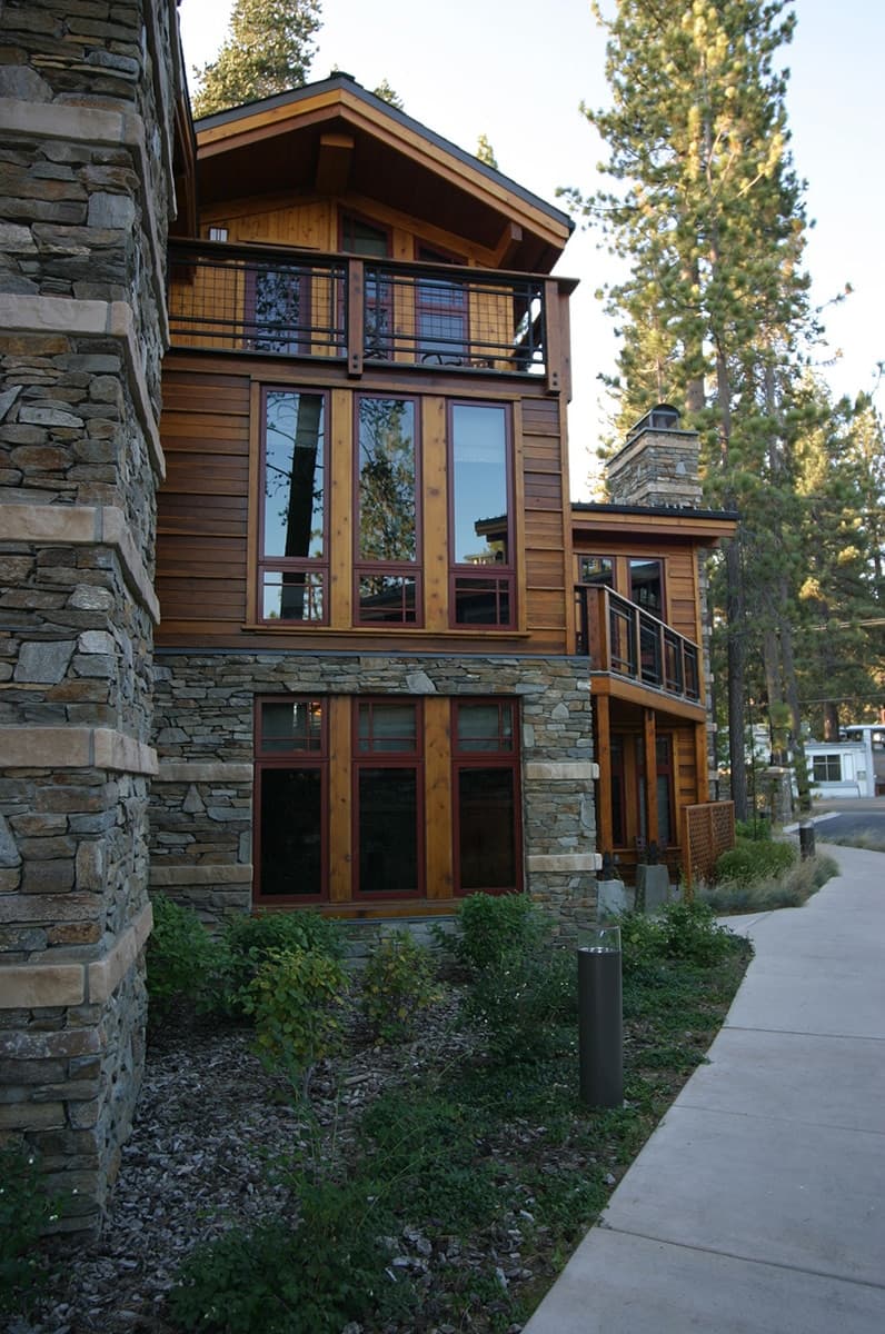 Stacked stone column and cedar-clad residence with tall windows beside a landscaped walkway